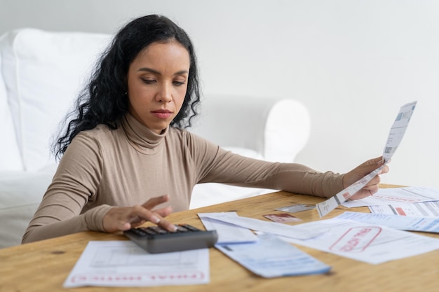 An individual meticulously reviewing household bills and expenses, using a calculator and a budget spreadsheet. The setting is a well-lit home office, emphasizing the importance of detailed financial planning.