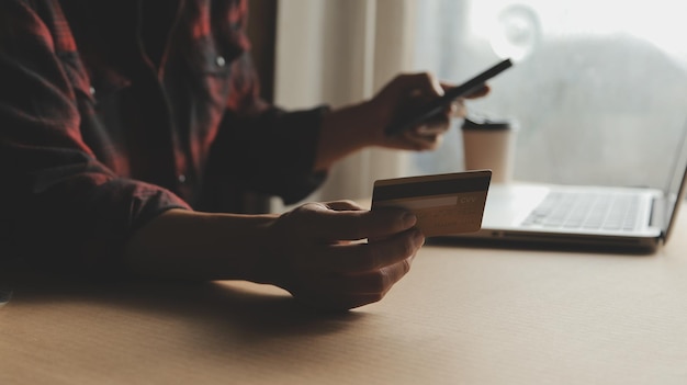 A person using a laptop and a smartphone simultaneously, comparing credit card interest rates on different websites. The scene is a brightly lit cafe.
