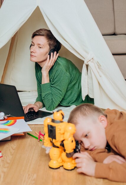 A person working on a laptop from home, surrounded by children's toys, symbolizing the working parent balancing work and childcare responsibilities. The scene is set in a brightly lit, comfortable environment, with financial documents visible in the background.