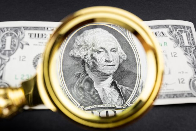 A close-up shot of a U.S. dollar bill with a magnifying glass over it, symbolizing the careful scrutiny of economic factors influencing inflation.