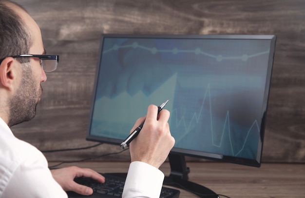 A close-up shot of the hands of a financial analyst reviewing data on a multi-monitor setup, with candlestick charts and Treasury yield curves visible on the screens. The analyst is wearing a professional suit and appears focused on interpreting the data.