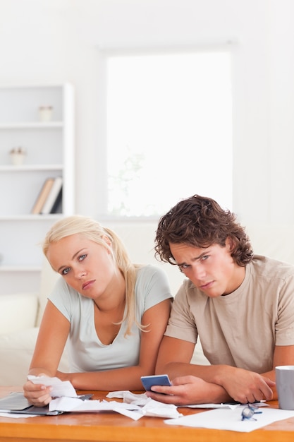 A young couple looking concerned while sitting at a table with mortgage documents. A calculator is visible on the table, suggesting they are assessing affordability.